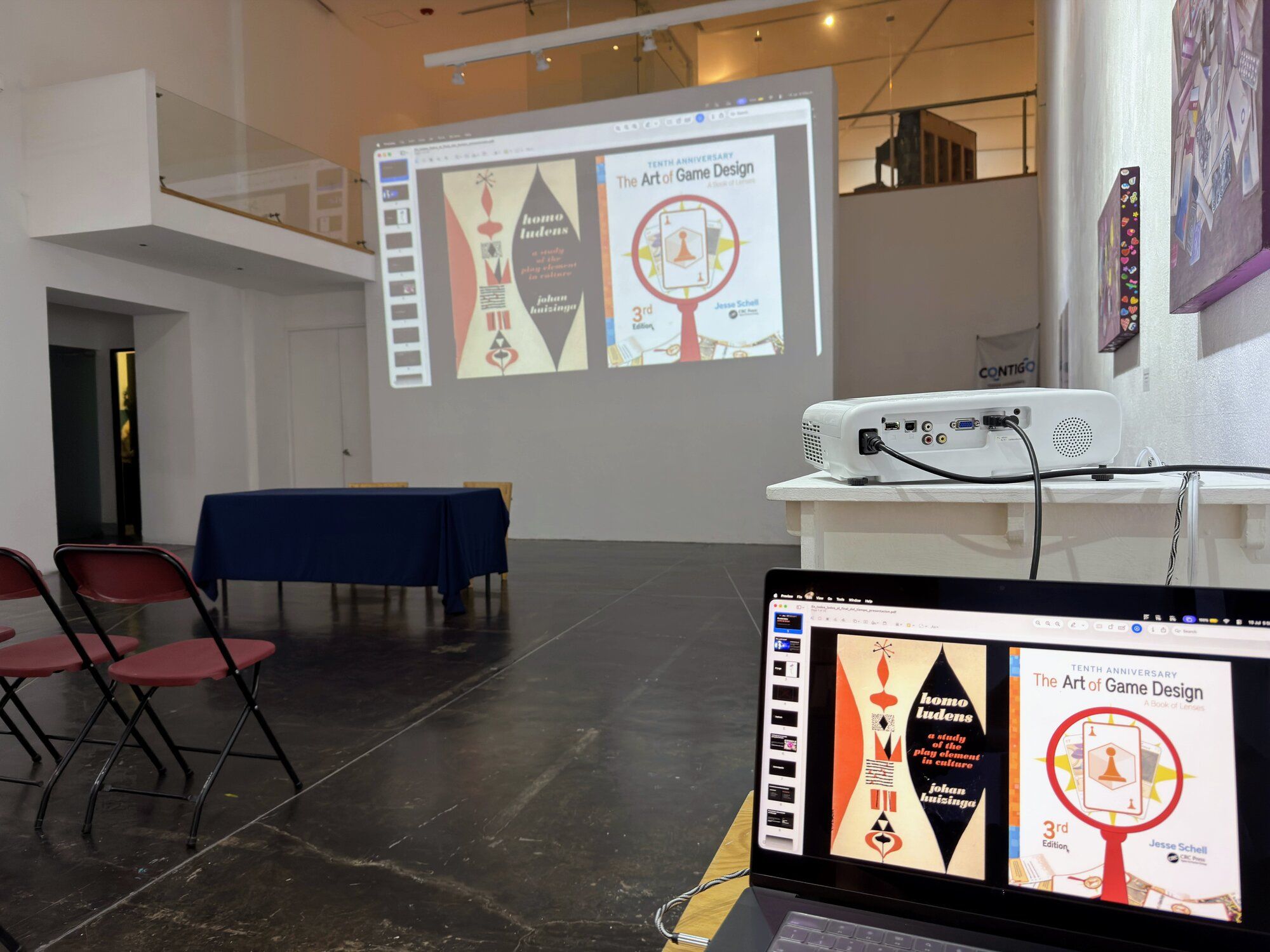 Presentation of En todos lados al final del tiempo at Galería Libertad, Querétaro: slides of Johan Huizinga's Homo Ludens and Jesse Schell's The Art of Game Design, projected in the gallery and mirrored on the laptop.